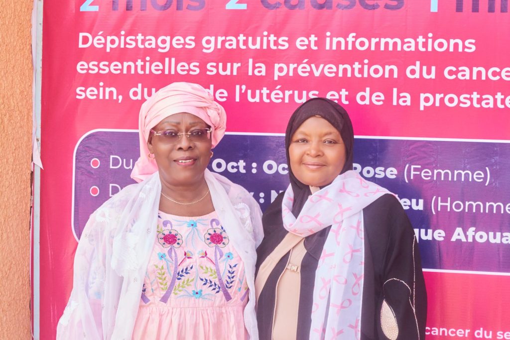 Deux membres de la délégation de la CONGAFEN devant l’affiche Octobre Rose et Novembre Bleu de la Clinique Afoua